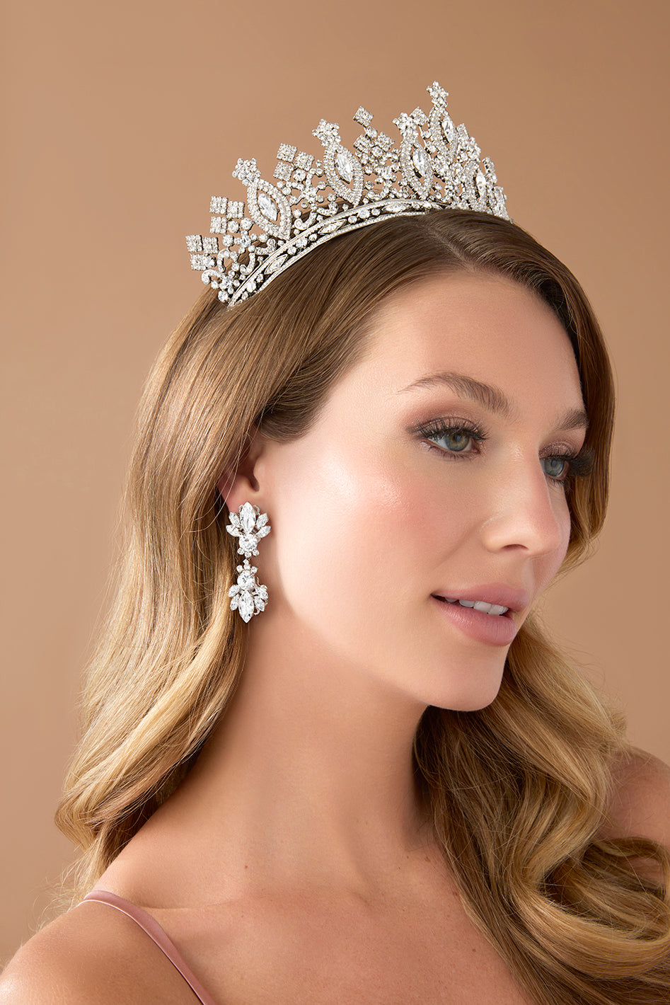 Woman wearing a sparkling crown and matching earrings against a beige background