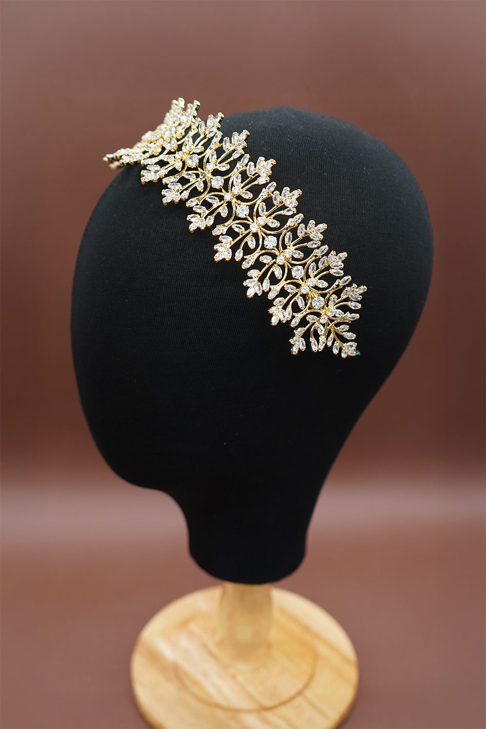Gold floral headband on a black mannequin head against a brown background